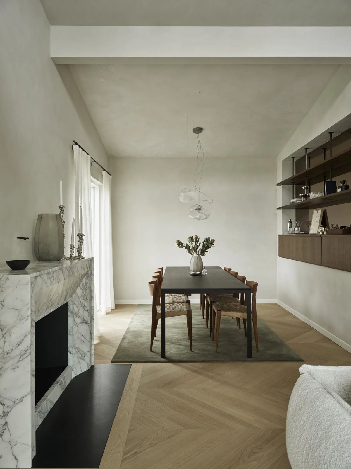 View from living room into dining space with marble fireplace, black table and wood chairs on green rug