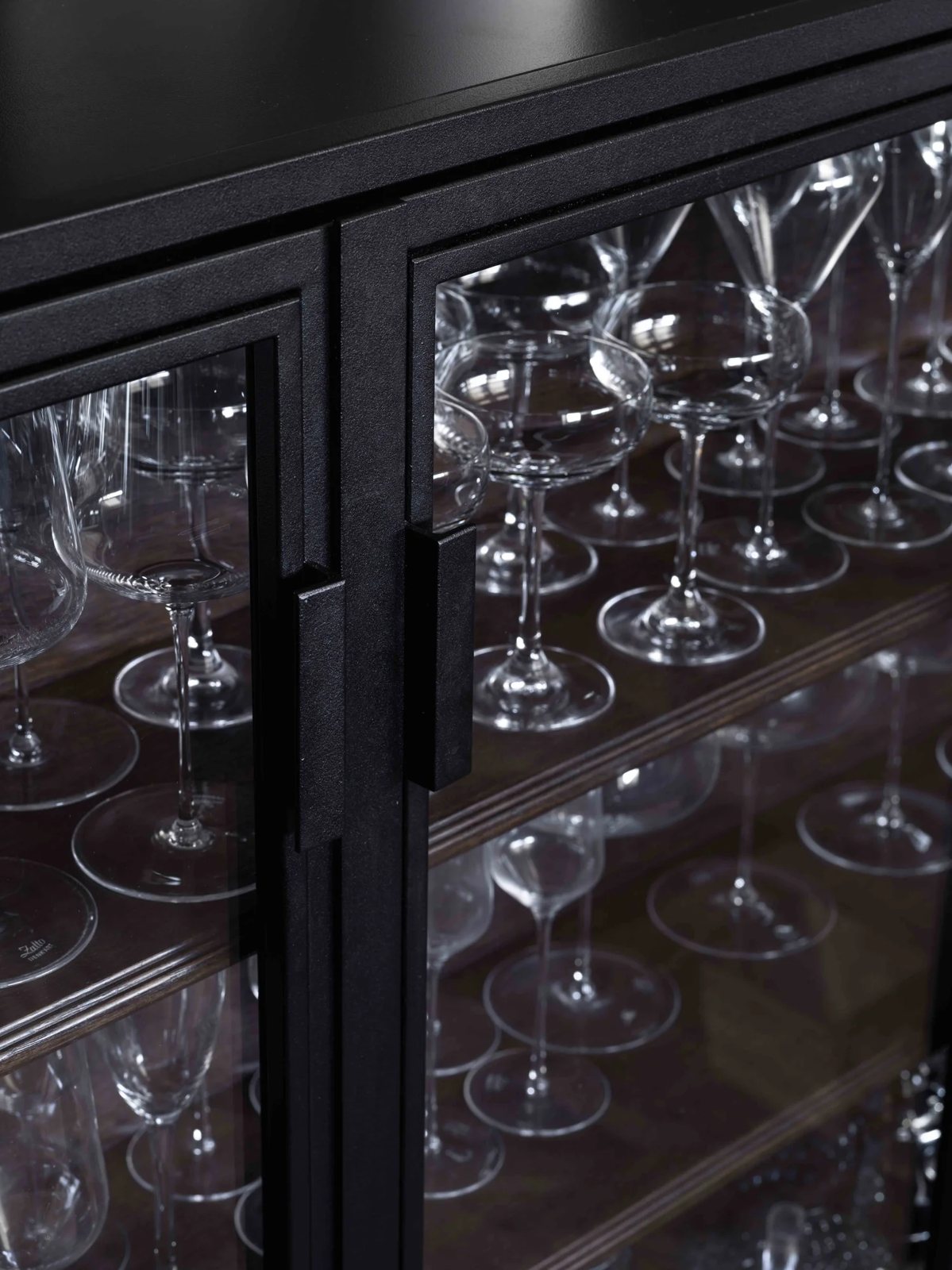 A close-up of a glass-fronted cabinet filled with fine wine and cocktail glasses arranged on wooden shelves.