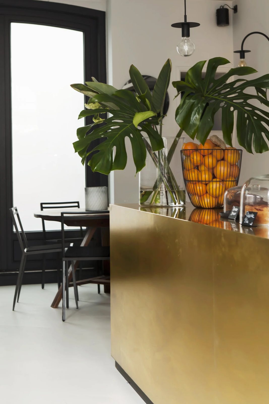 Brass café counter with fruit bowl and leafy plants.