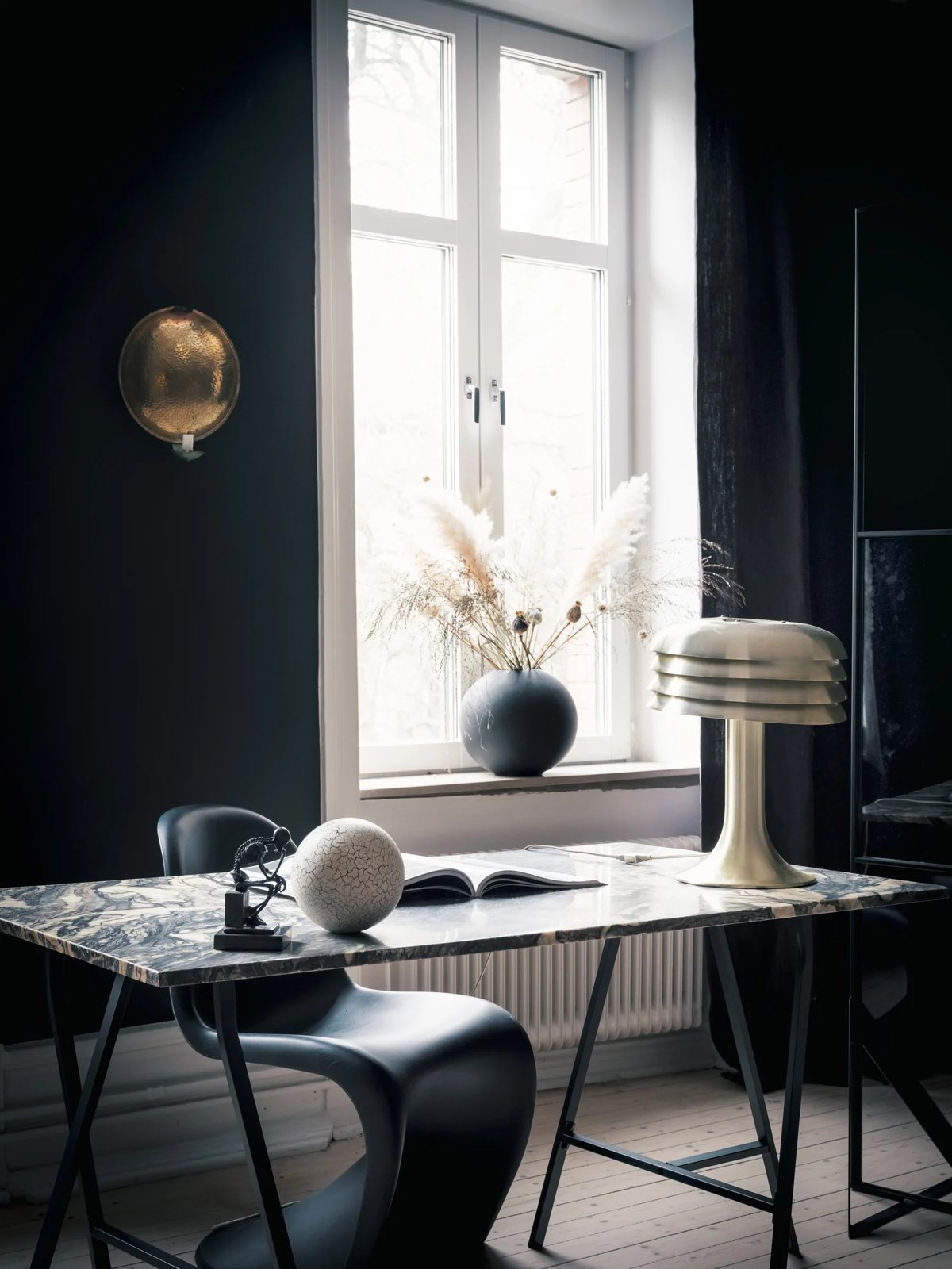 Black Panton chair and brass lamp by a veined marble desk under daylight.