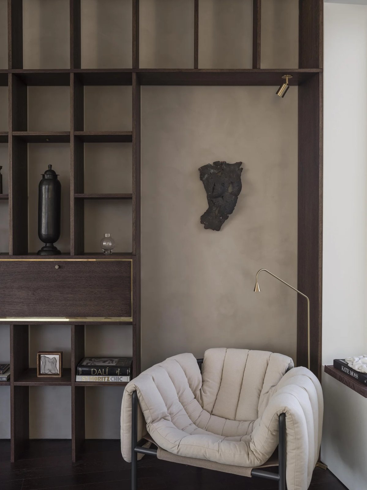 Cozy armchair next to built-in oak bookshelf with art and books