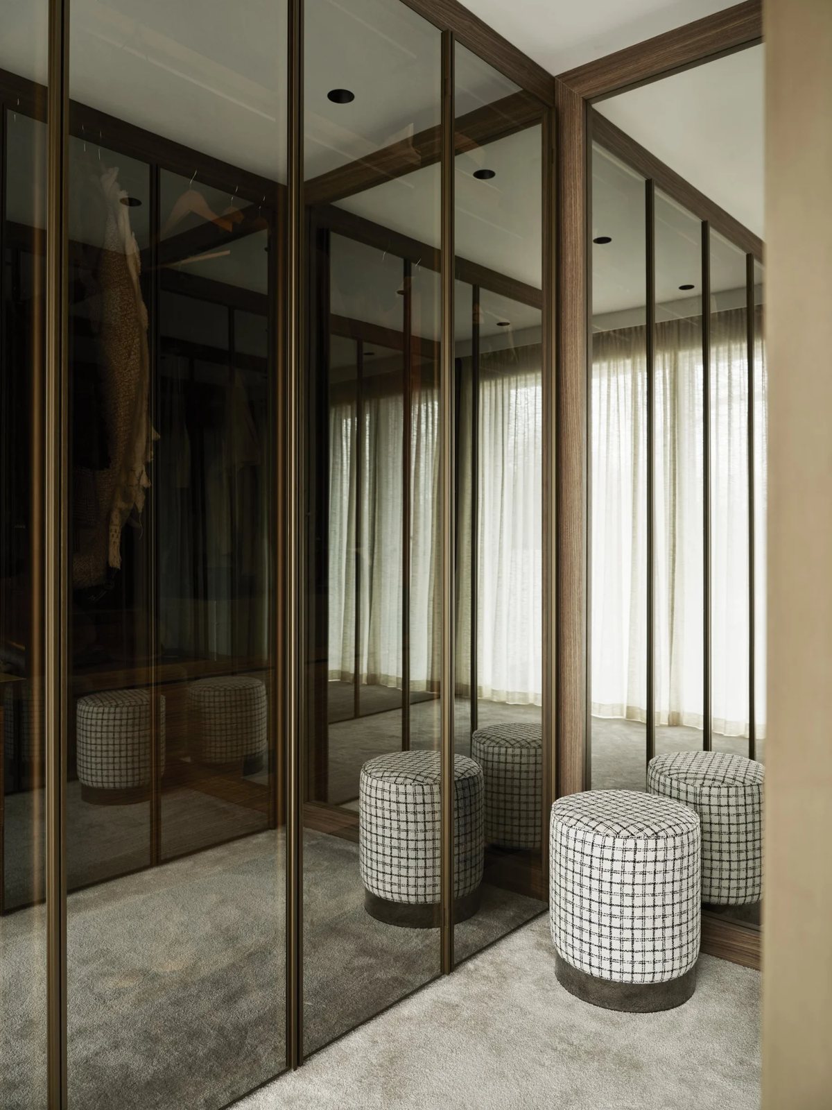 Mirrored wardrobe with bronze frame and patterned poufs on soft carpet
