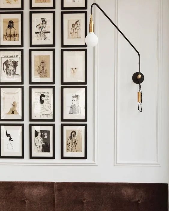 Framed sketches and brass wall lamp over velvet bench.