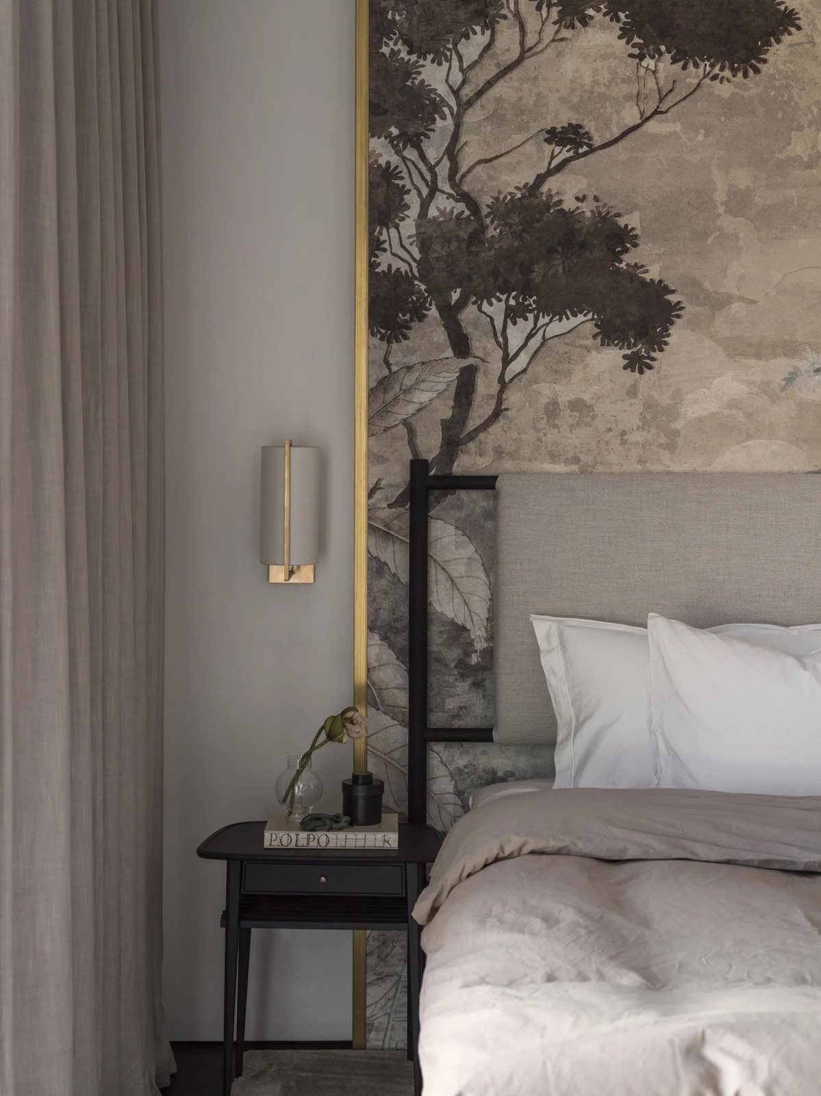 Close-up of a cozy bed set against a botanical mural wallpaper, featuring soft textiles and warm lighting