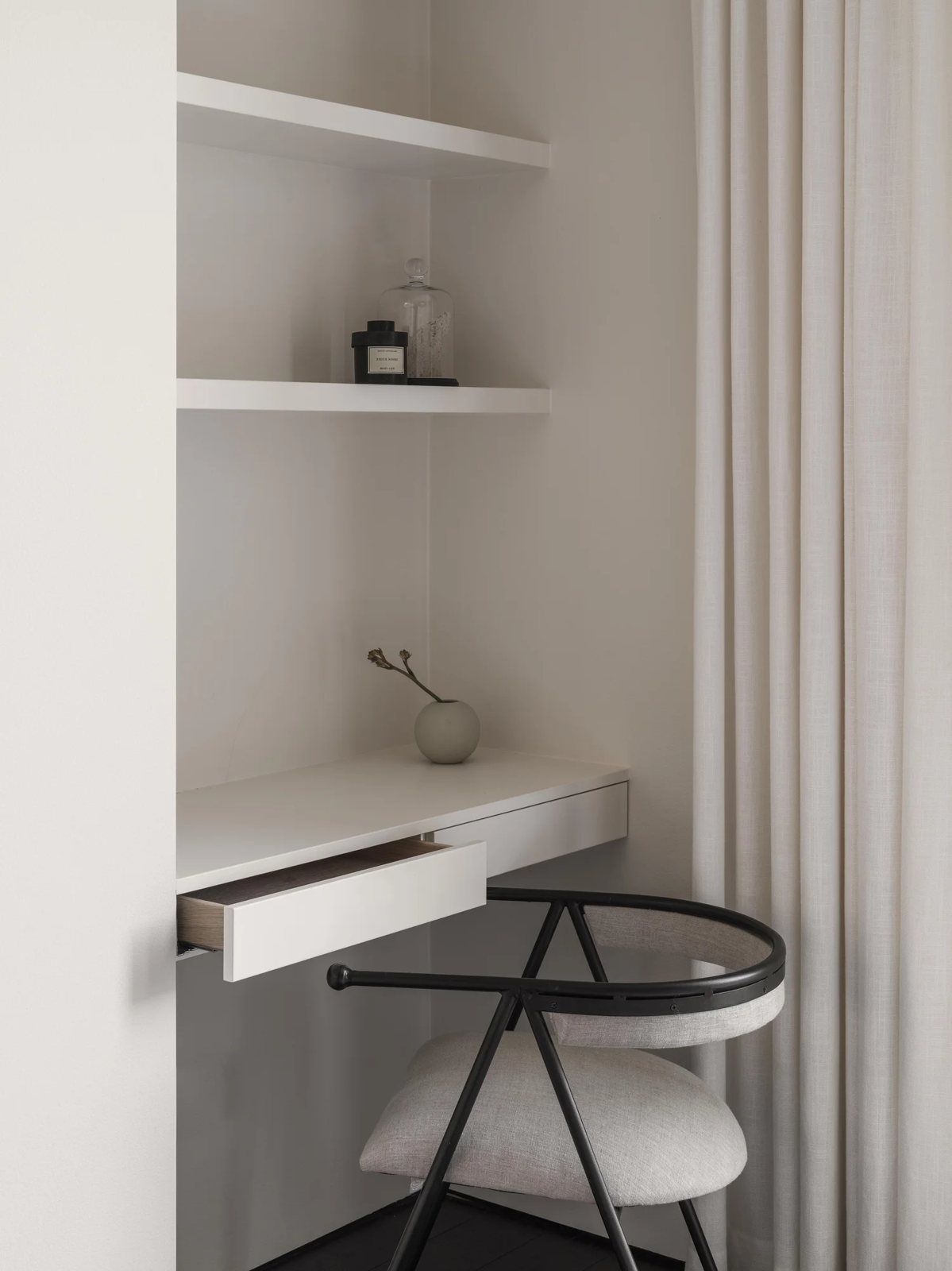 Minimal built-in white desk nook with sculptural upholstered chair and open shelves.