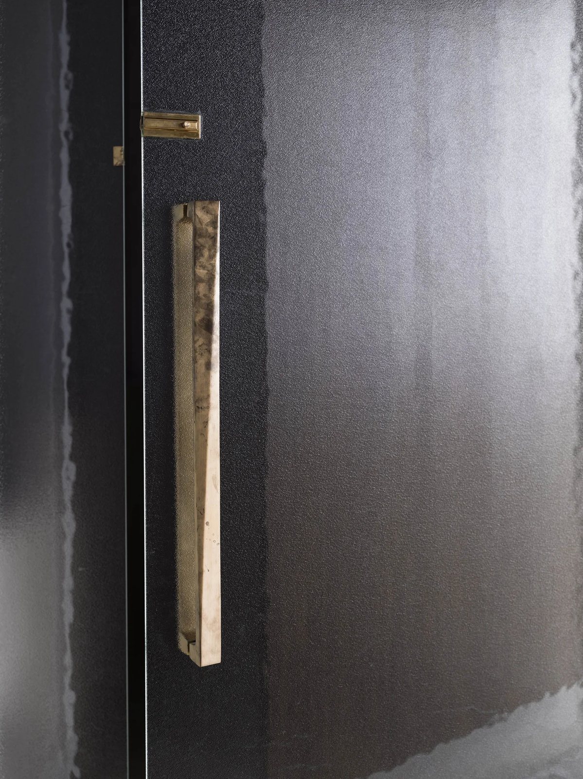 Detail shot of a rippled glass door featuring elegant brass hinges and a textured bronze handle.
