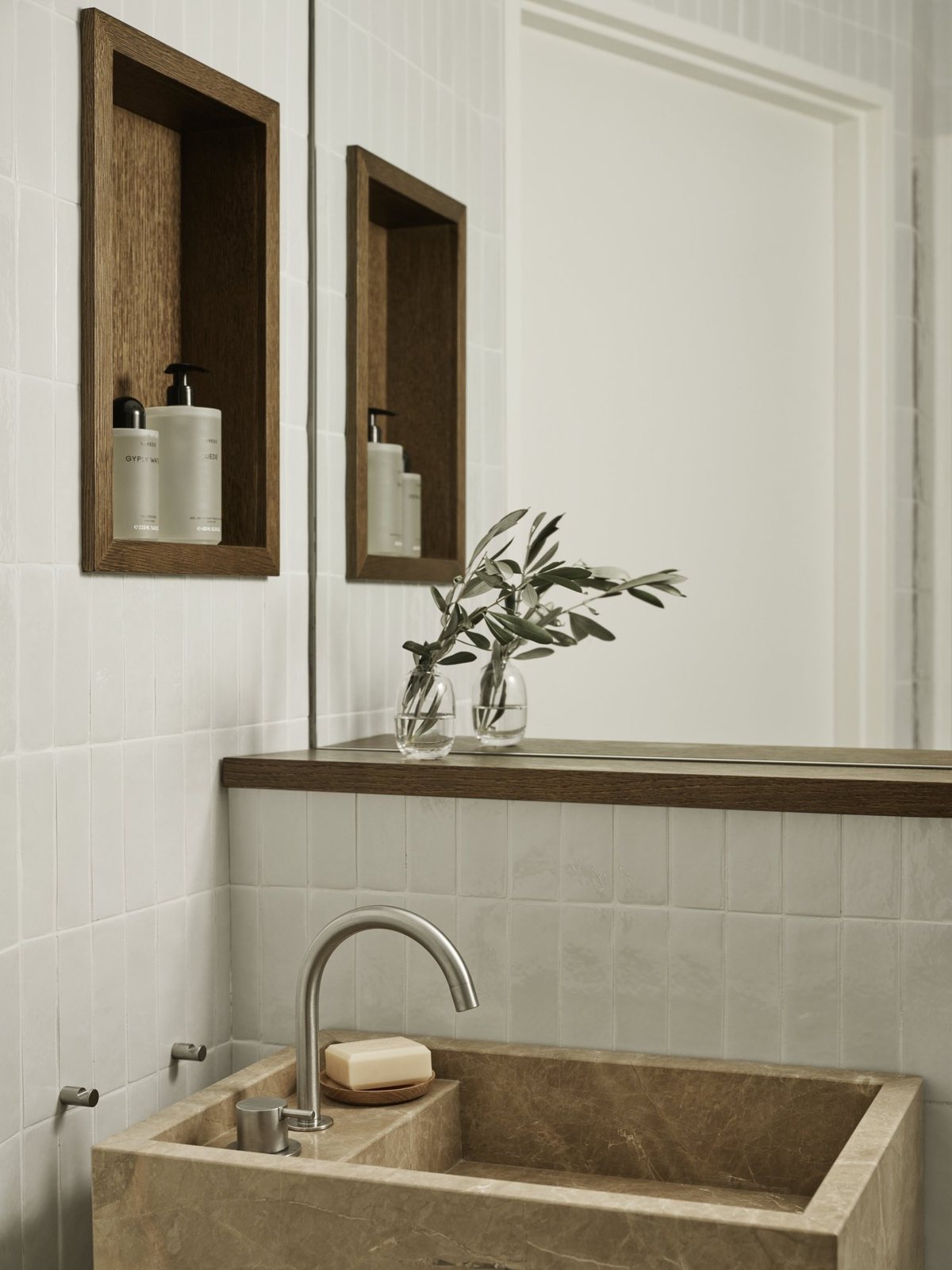 A guest powder room featuring a monolithic natural stone sink, zellige wall tiles, and a recessed oak shelf for toiletries.