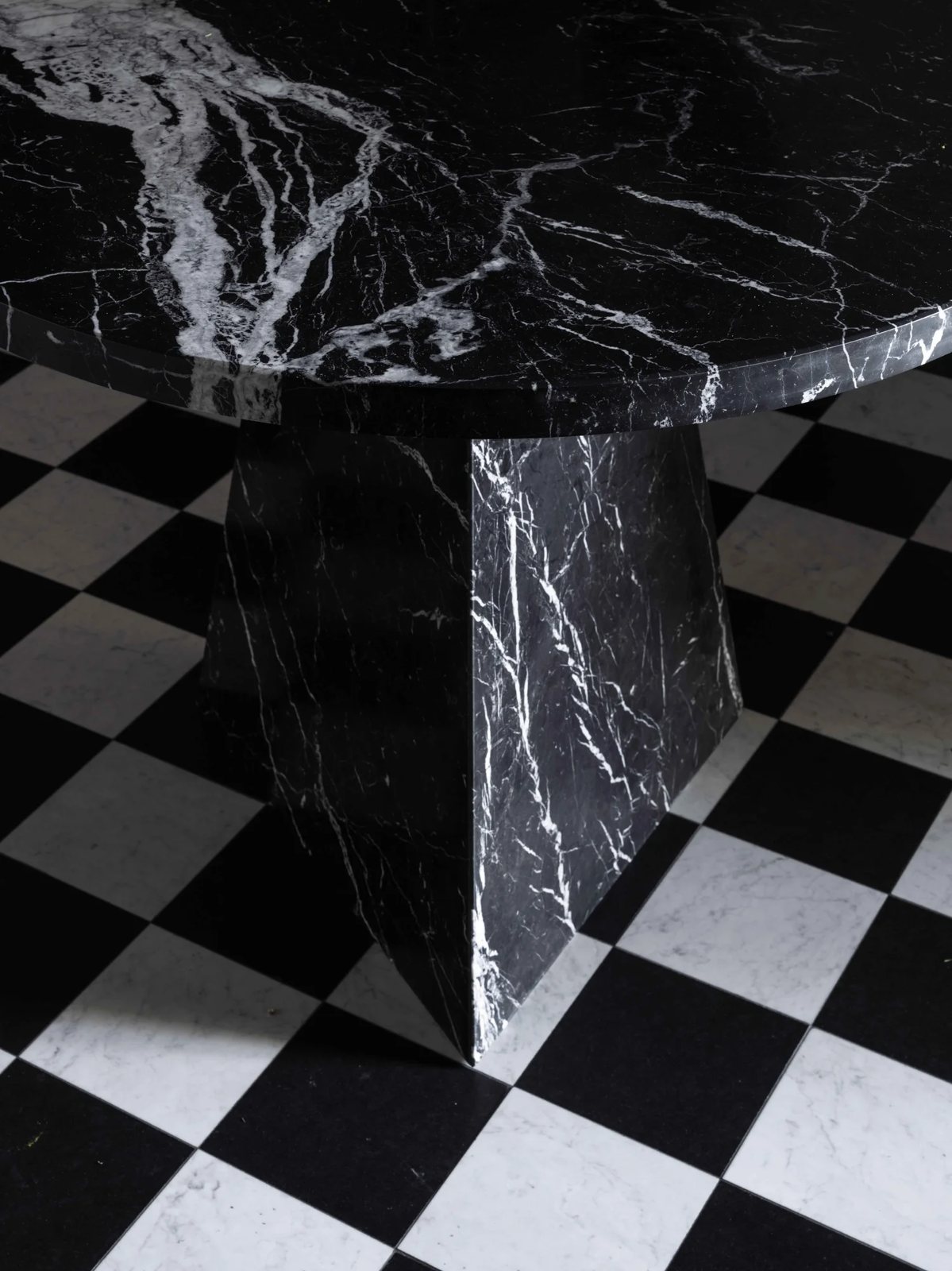 A sculptural black marble table with striking veining, placed on a bold black and white chequered floor.