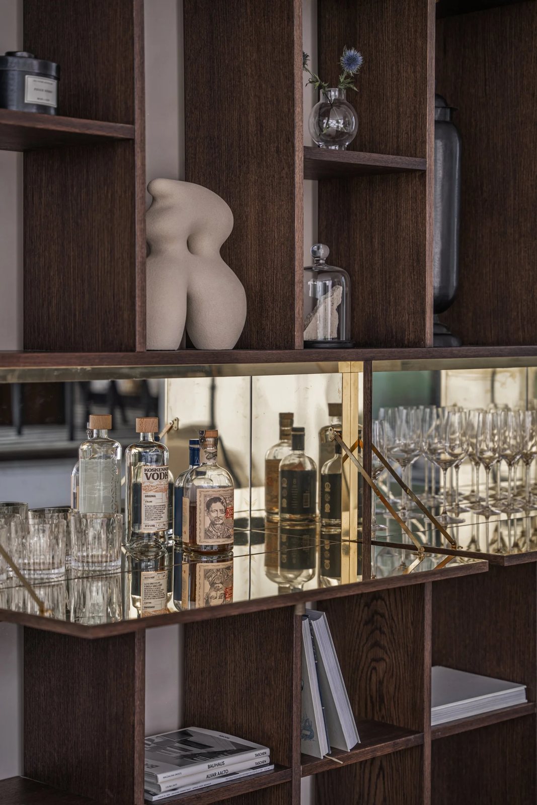 Close-up of a bespoke bar cabinet with mirror, brass trim, and a curated selection of spirits and glassware.