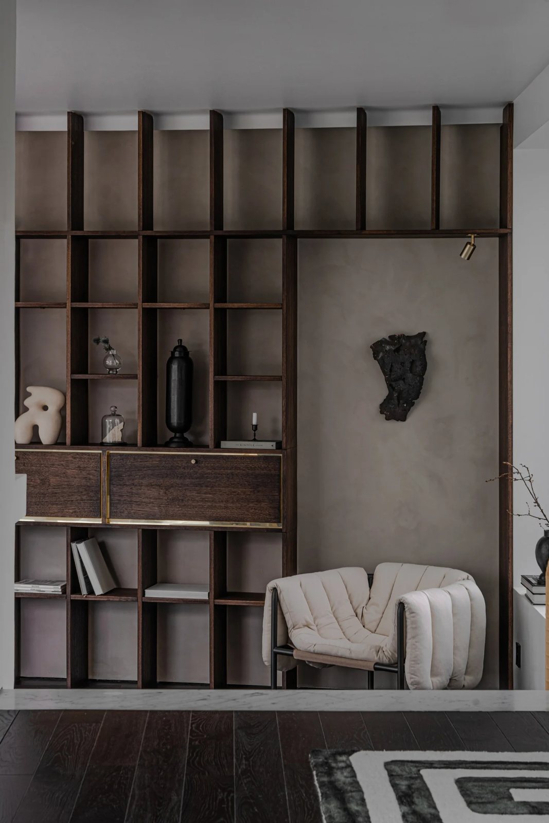Dark oak shelving system with brass accents and sculptural chair