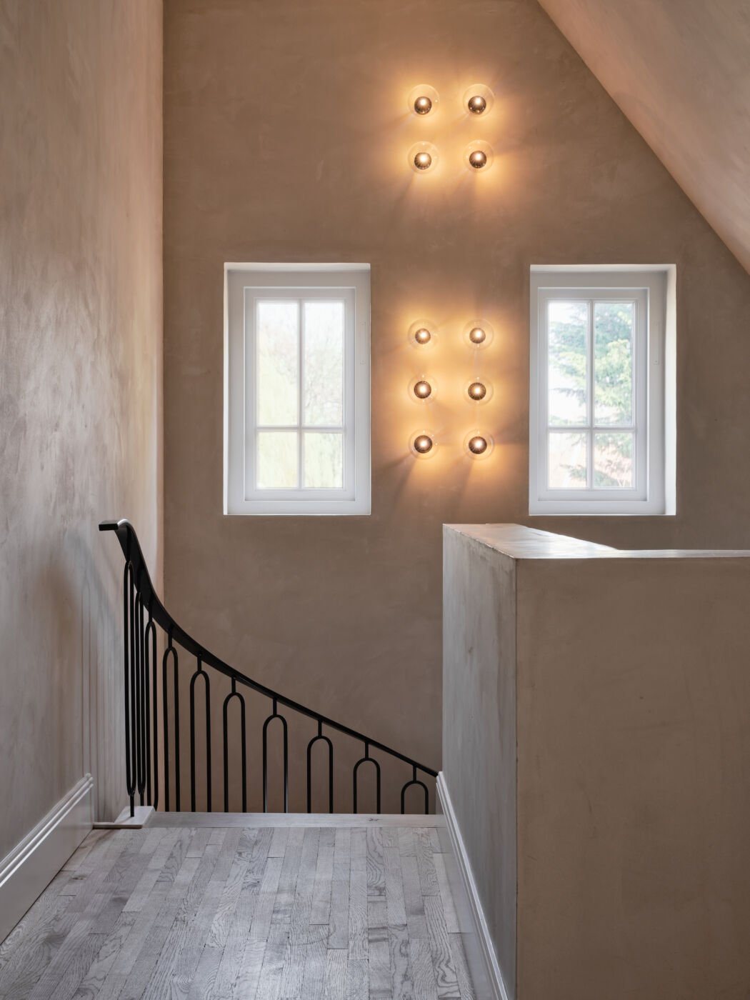 A softly lit stairwell with plaster-finish walls and decorative wall lights arranged in a grid above the stairs.