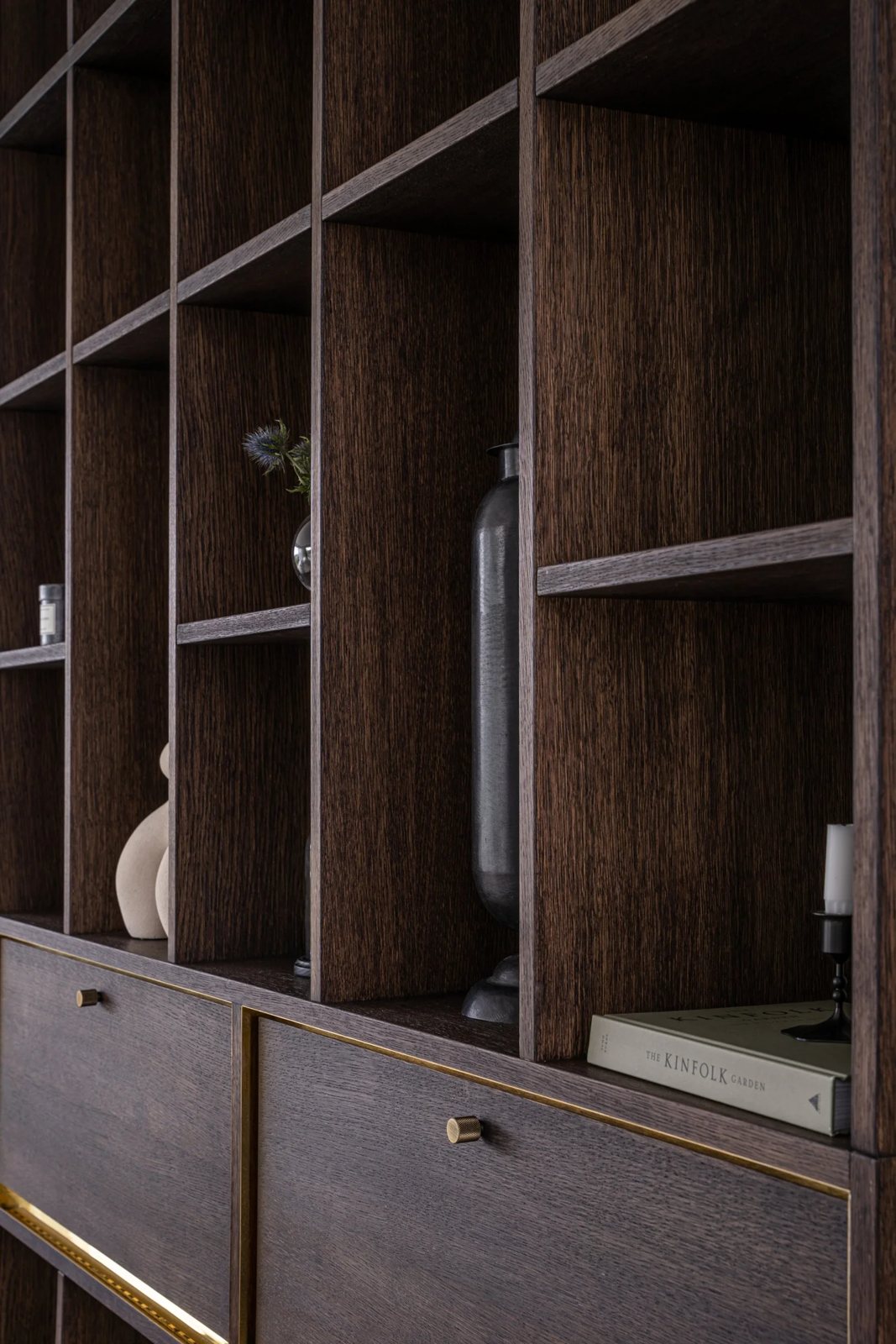 Vertical shelves in dark oak with decorative objects and brass accents