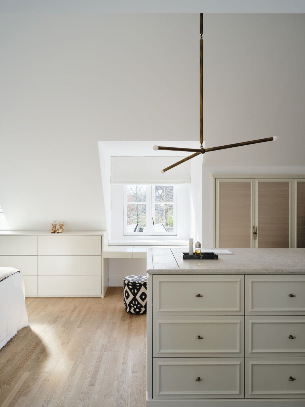 A custom-designed walk-in closet featuring painted drawers, a central island with limestone top, and a geometric pendant light.