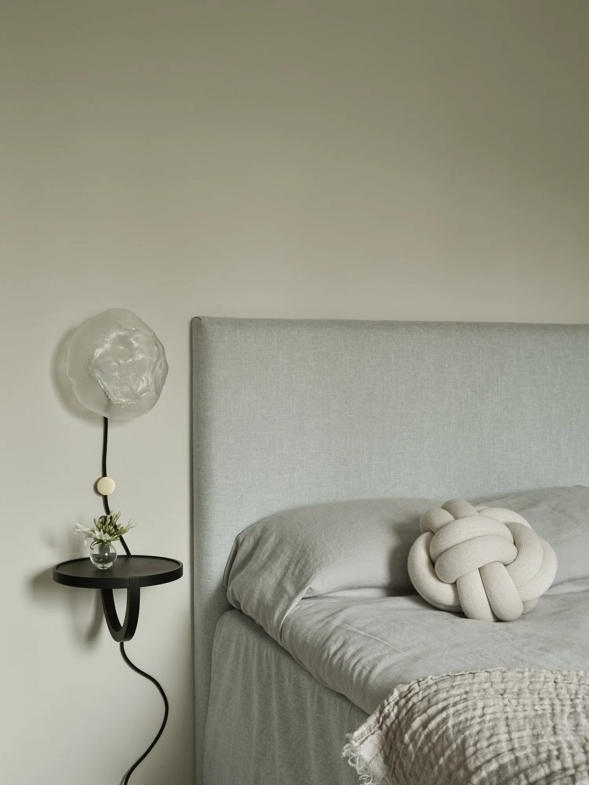 Green upholstered bed with glass lamp and knot pillow