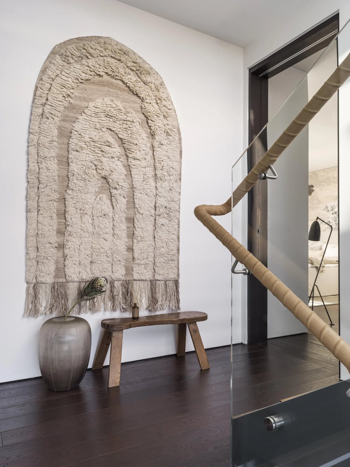 Entrance with arched hanging wool wall art, rustic wooden bench and ceramic vase on dark wood floors.