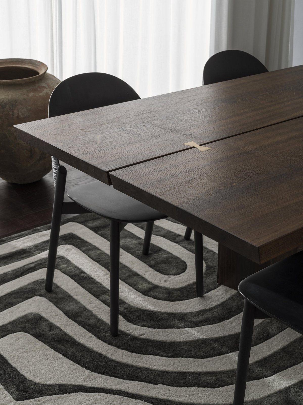 Detail of a dark oak dining table with visible butterfly joint, set against a black-and-white graphic rug.