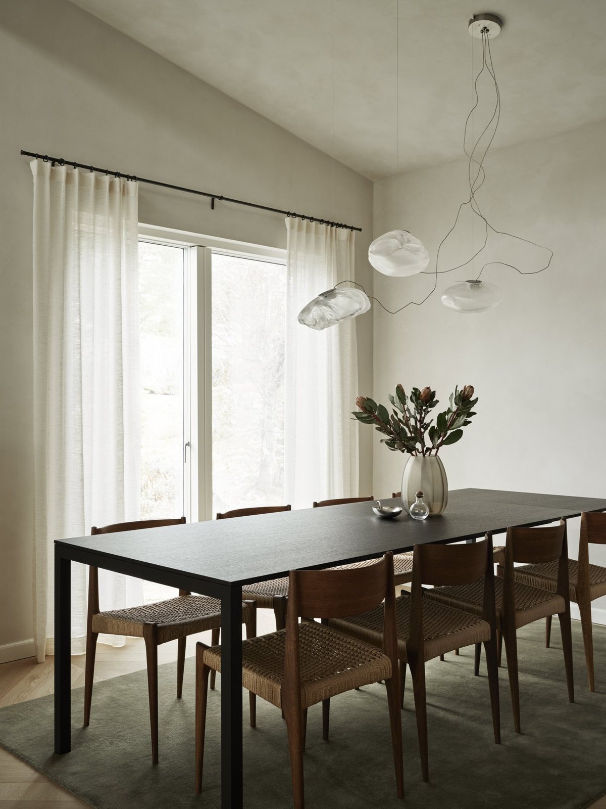 Minimalist dining room with sculptural pendant lights, black dining table and vintage wood chairs on oak chevron flooring