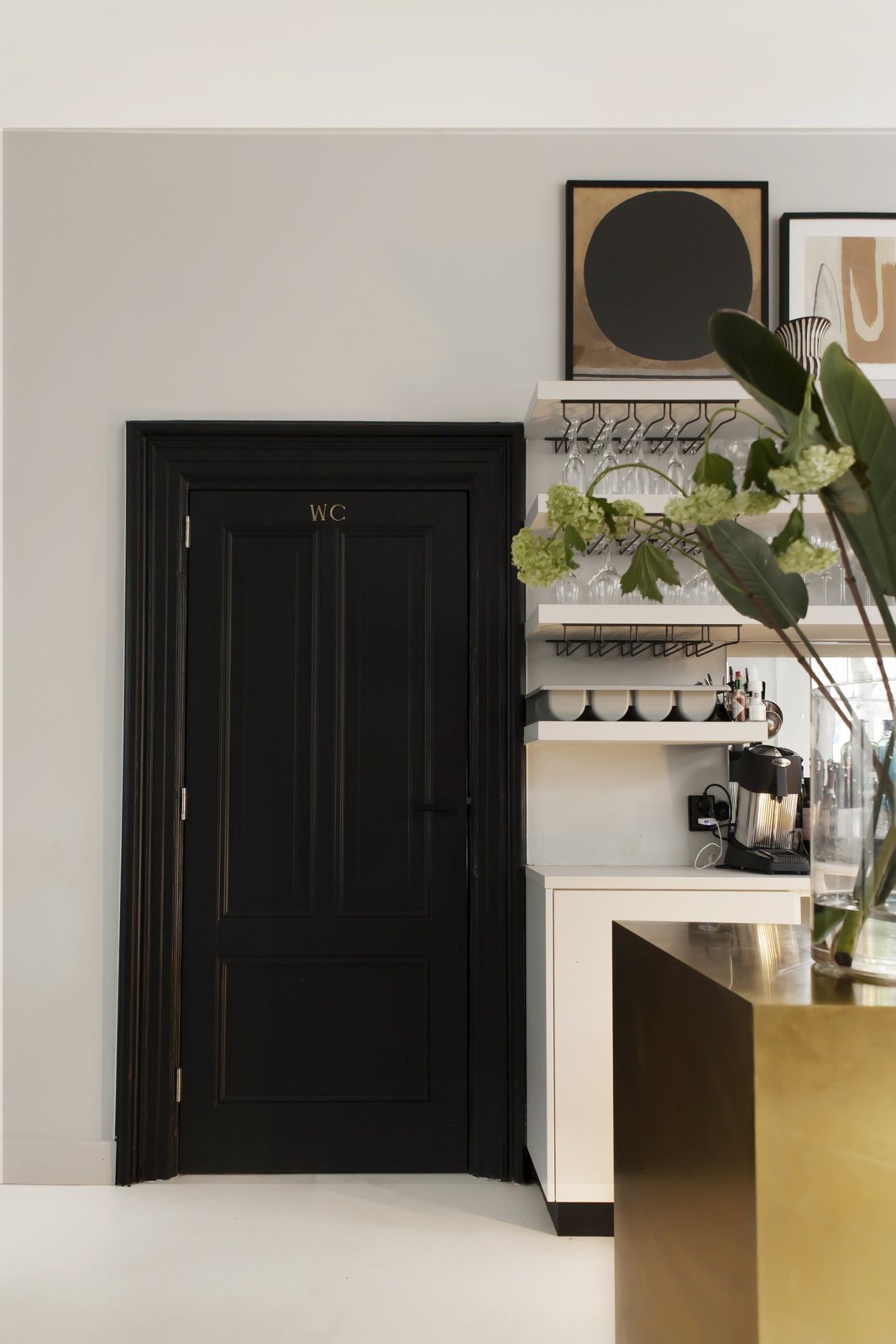Brass bar, open shelves with glasses, and black WC door.