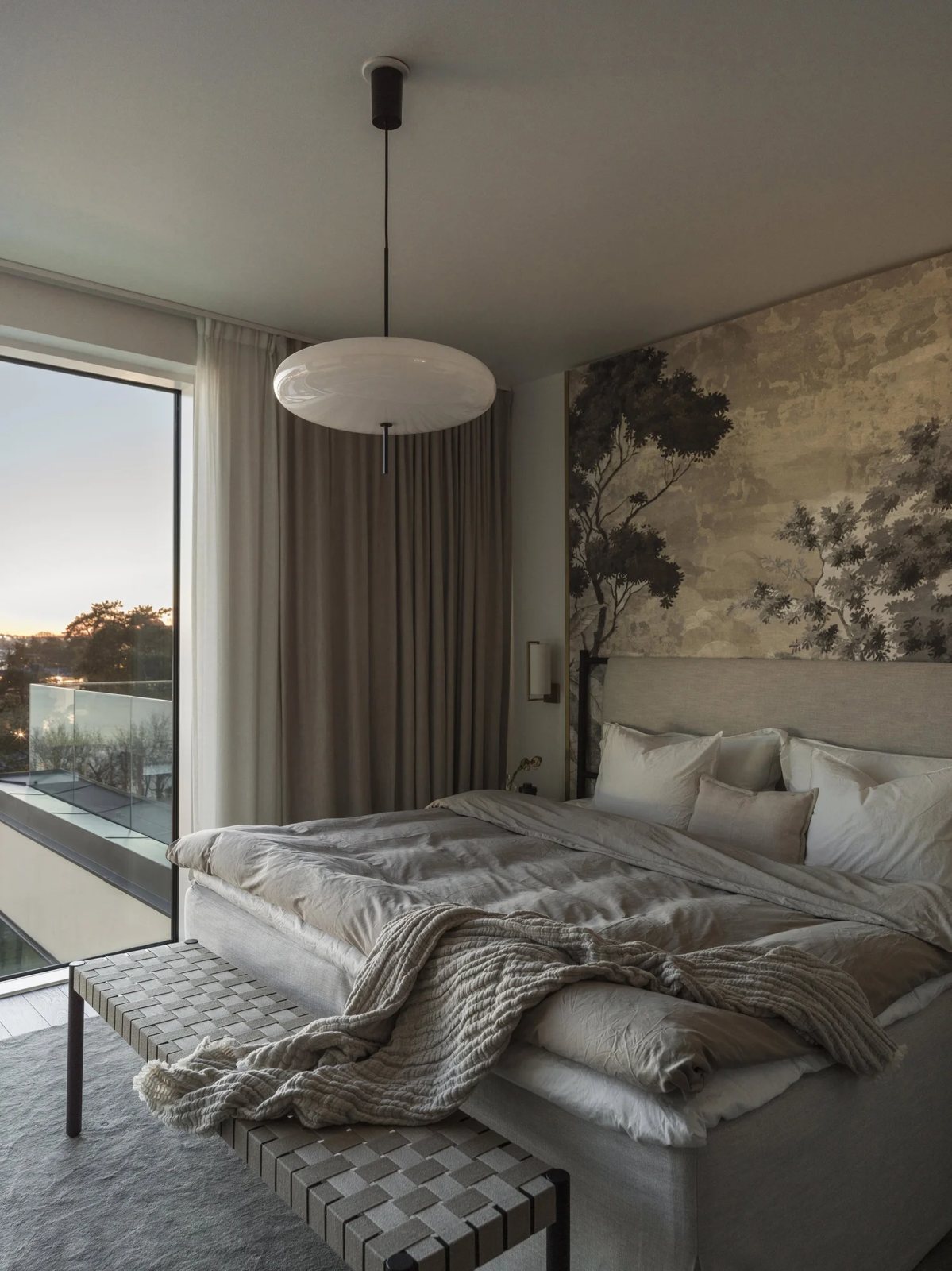 A serene bedroom featuring floor-to-ceiling curtains, a nature-inspired wall mural, and soft layered bedding.