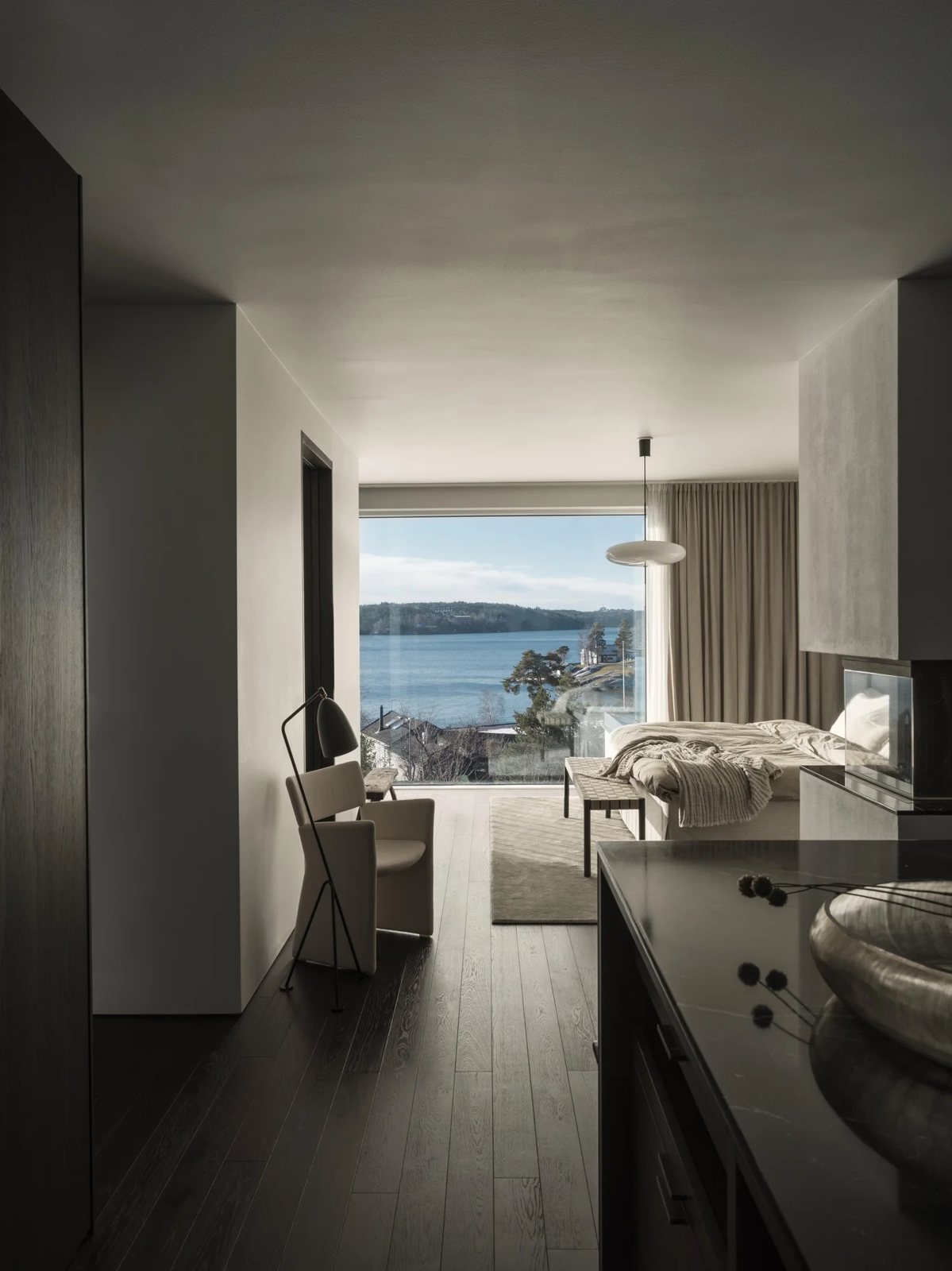View from walk-in-closet into bedroom with lake view, accent chair, and layered lighting.
