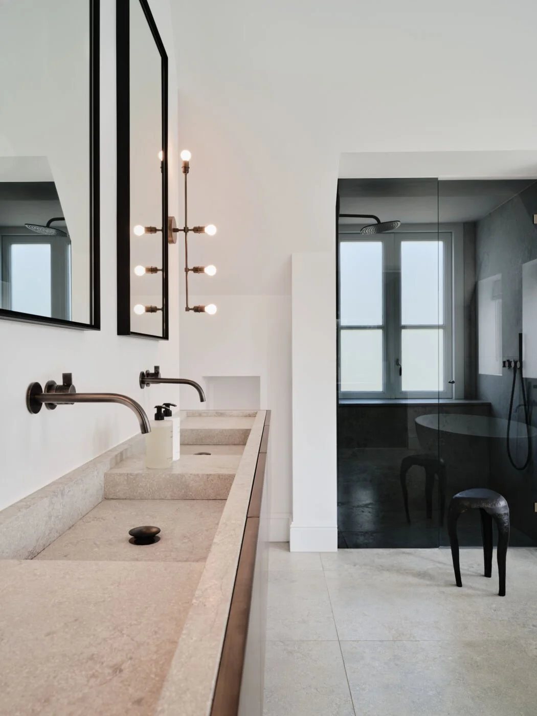 Close-up of a limestone vanity with brushed brass fixtures and a frameless glass shower enclosure in the background.