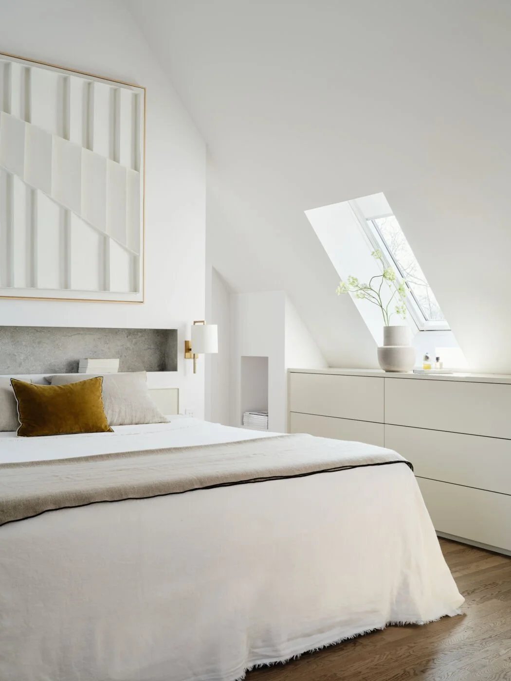 White attic bedroom with skylight and geometric art.