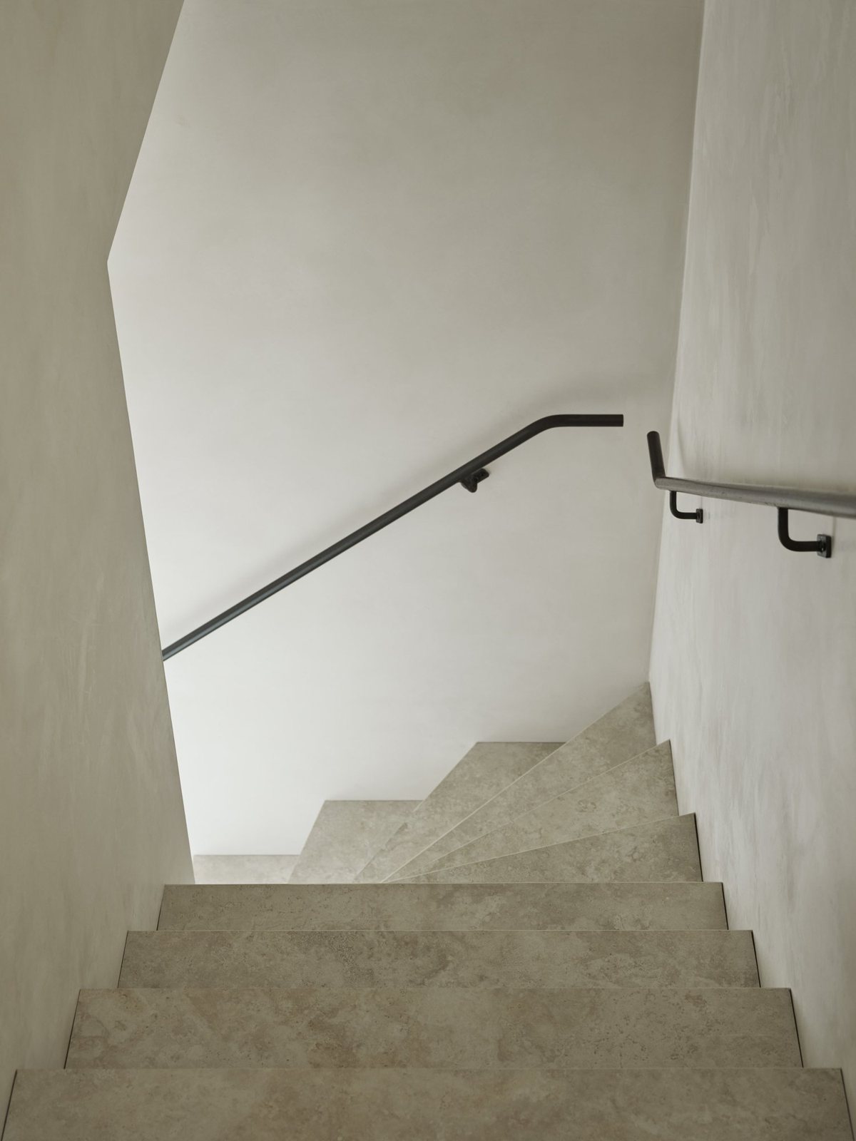 Limestone stairs with minimalist metal railing and soft-toned plaster walls