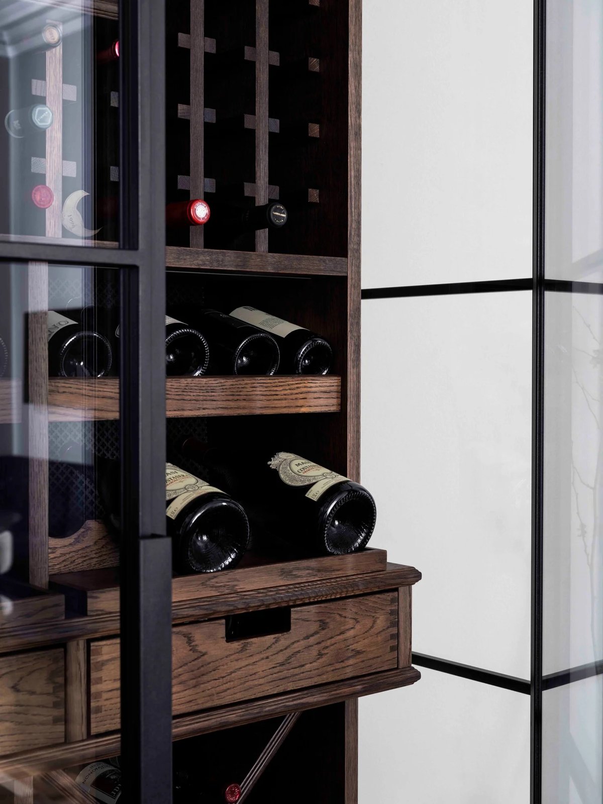 A close-up of a bespoke wine cabinet in dark oak with bottle racks and a drawer, framed by glass doors.