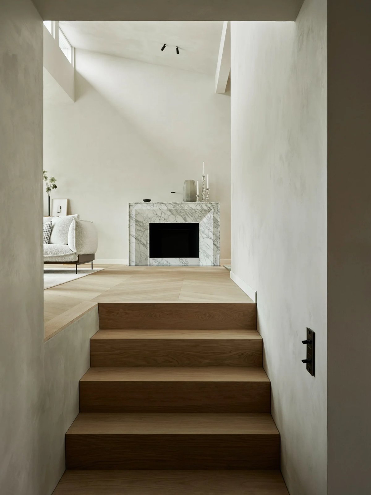 Light-filled view from oak staircase into calm living space with marble fireplace