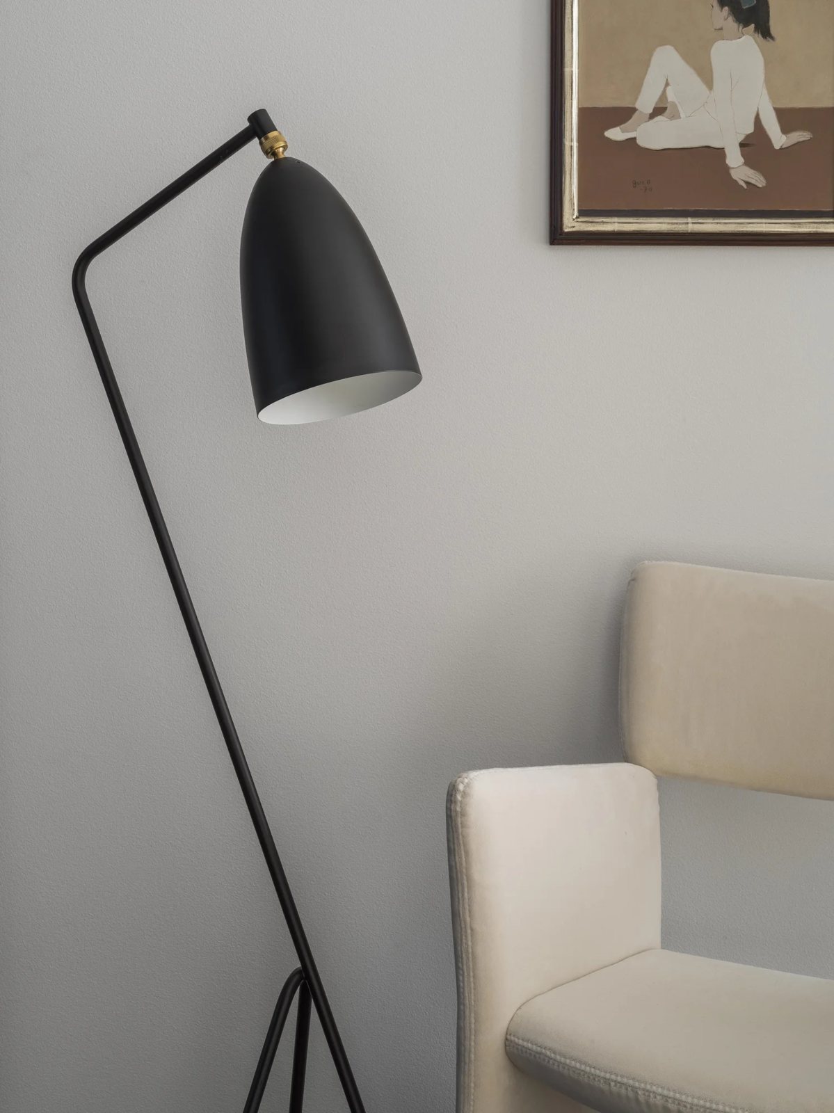 Close-up of a minimalist reading nook with a sculptural floor lamp, cream chair and wall art.